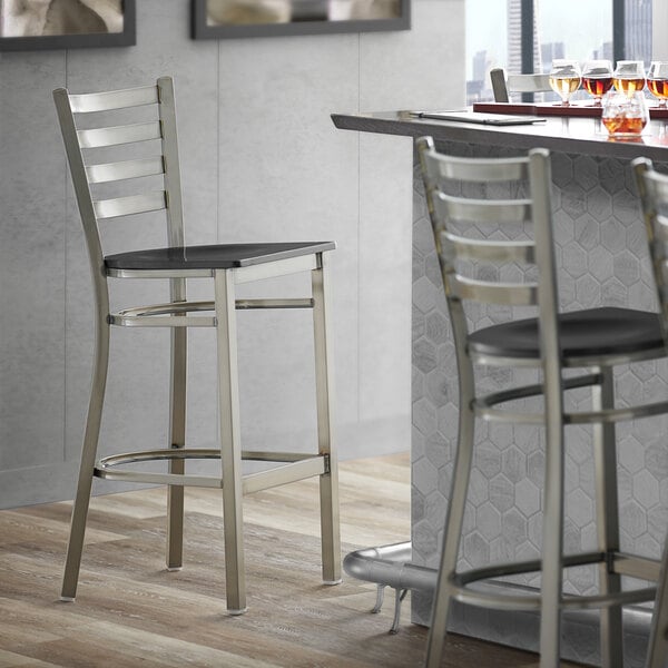 A Lancaster Table & Seating ladder back bar stool with a black wood seat.