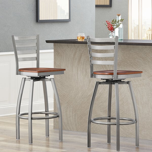 Two Lancaster Table & Seating Ladder Back Swivel Bar Stools with wooden seats at a bar.