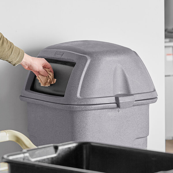 A person throwing a paper in a Toter graystone square dome lid on a 35 gallon slimline trash can.