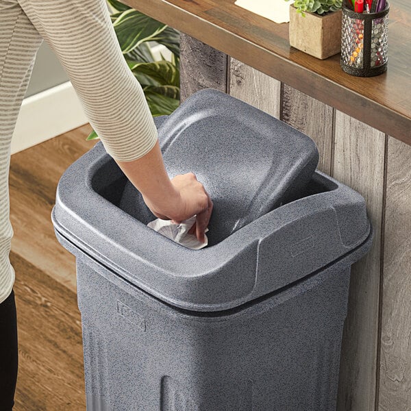 A woman's hand putting a Toter graystone lid on a trash can.