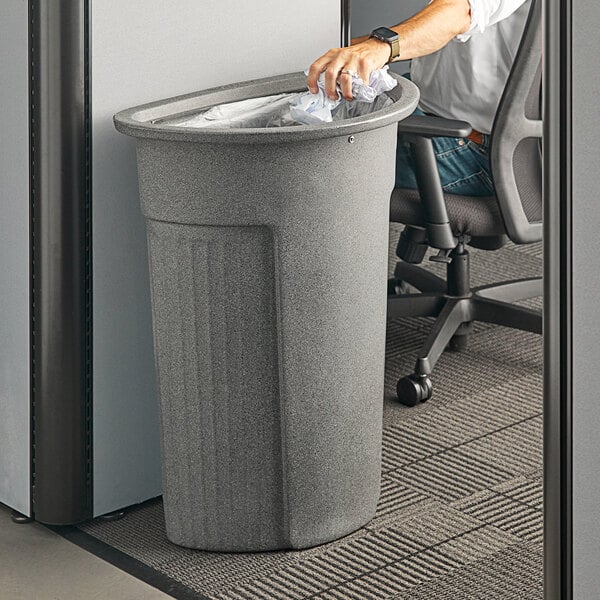 A man putting a plastic bag in a Toter Slimline half round trash can in a corporate office cafeteria.