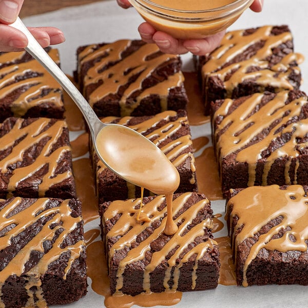 A hand pouring REESE'S smooth peanut butter onto a brownie.