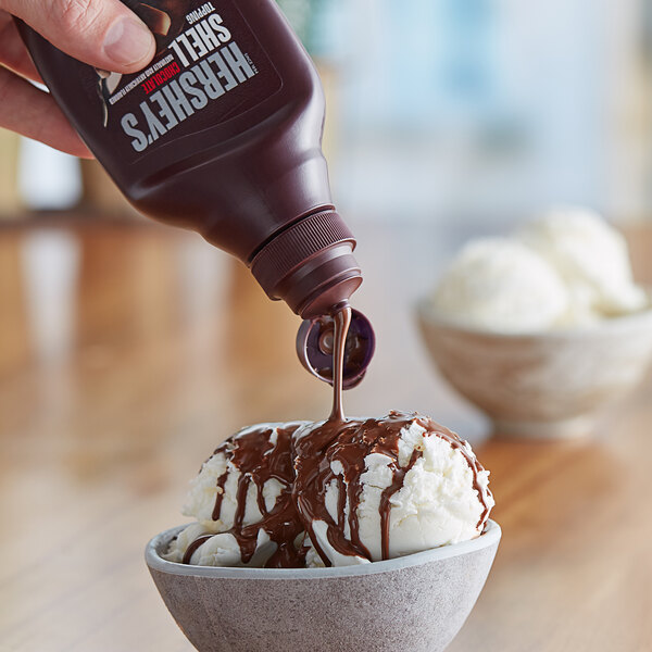 Hershey's chocolate shell topping being poured over a bowl of ice cream.