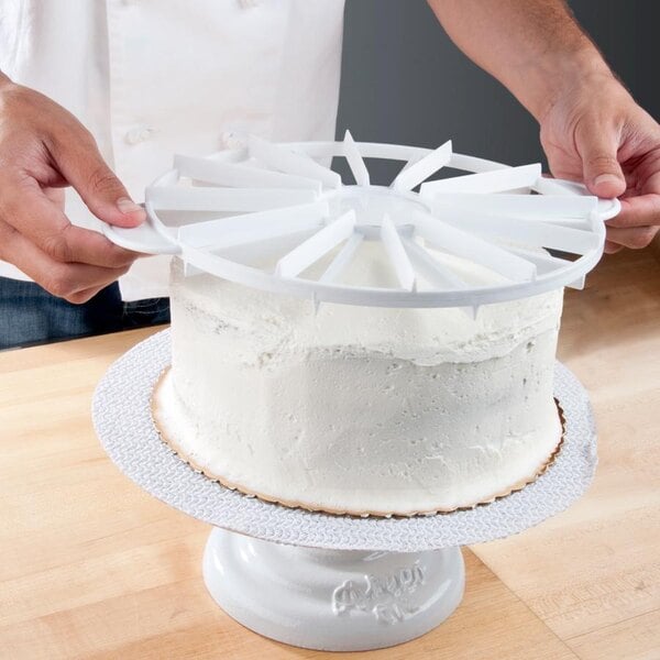 A person using an Ateco double-sided white plastic cake marker to cut a white cake.