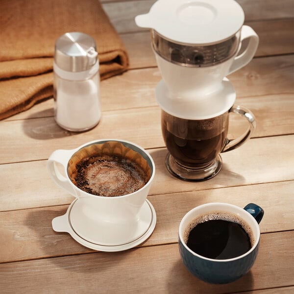 An OXO pour over coffee maker with a cup of coffee on a table.