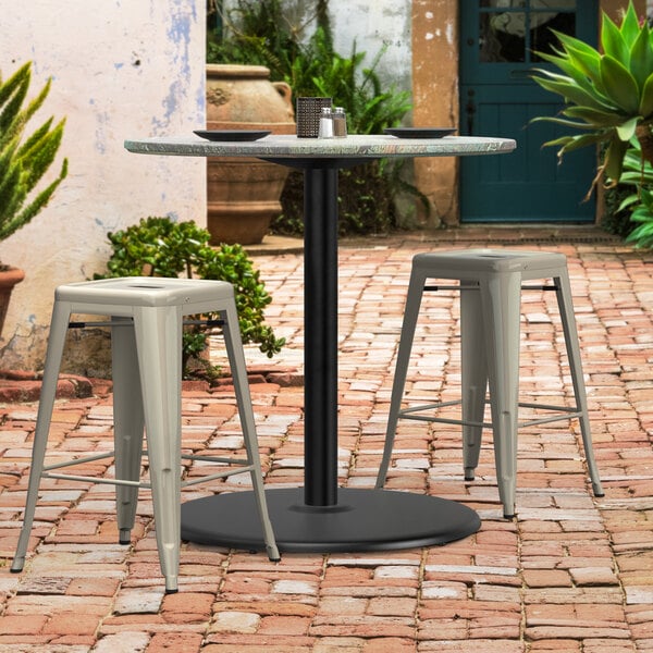 A Lancaster Table & Seating black outdoor table base with stools on a brick patio.