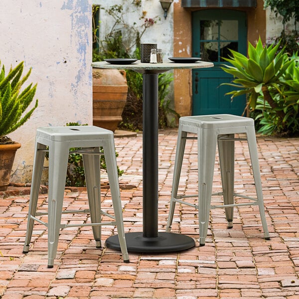 A Lancaster Table & Seating black outdoor table base with a counter height column on a table with plates and a container on a brick patio.