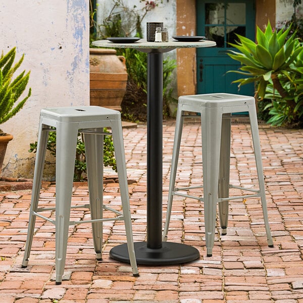 A Lancaster Table & Seating black table base with bar stools on a brick patio.