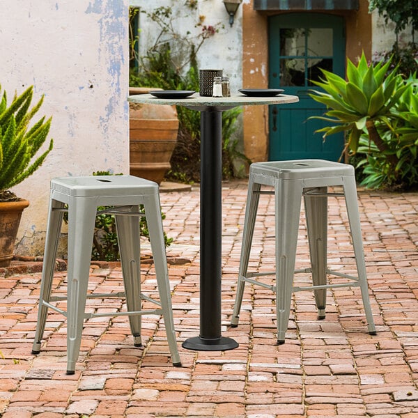 A Lancaster Table & Seating black outdoor table base with a pair of stools on a brick patio.