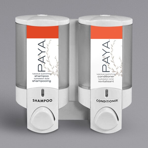 A white Dispenser Amenities wall-mounted soap dispenser with two translucent bottles and a white Paya label.