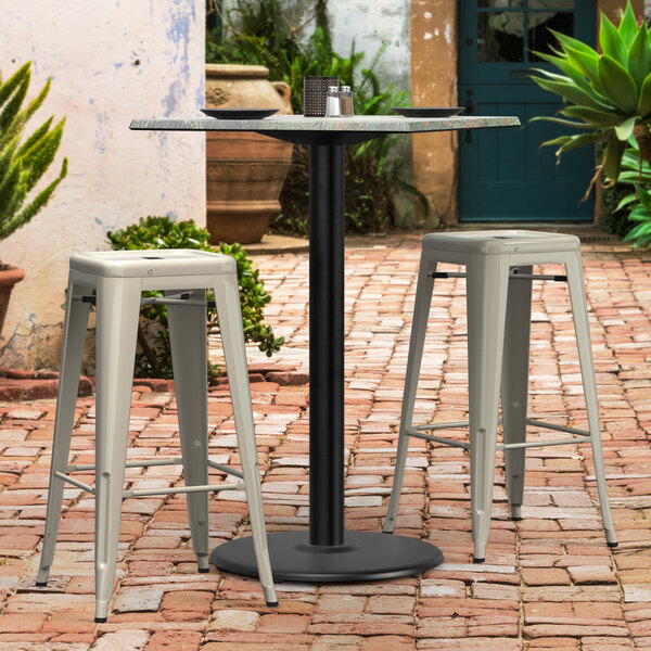 A Lancaster Table & Seating black outdoor table base with bar stools on a brick patio.
