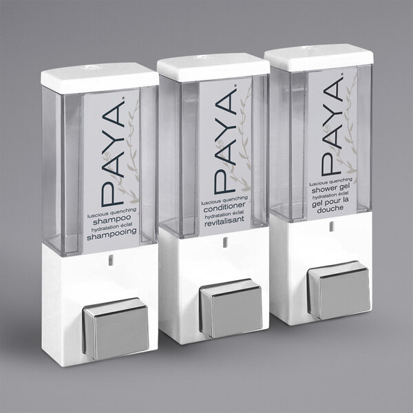 A white wall mounted Dispenser Amenities Paya shower dispenser with three translucent bottles and a Paya logo.