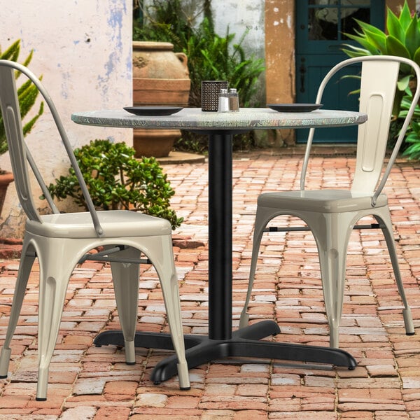 A Lancaster Table & Seating black outdoor table base with chairs on a brick patio.