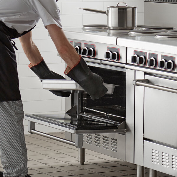 A man in a chef's outfit using black gloves to put food in a stainless steel Garland restaurant oven.