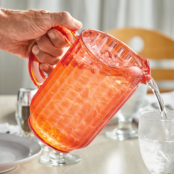 A person pouring water from a plastic bag into a Choice coral plastic beverage pitcher.