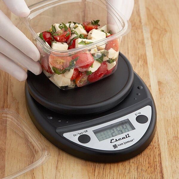 A person weighing food in a plastic container on a San Jamar Escali kitchen scale.