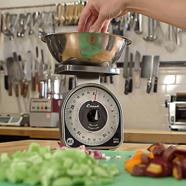 A hand weighing vegetables on a San Jamar Escali kitchen scale.