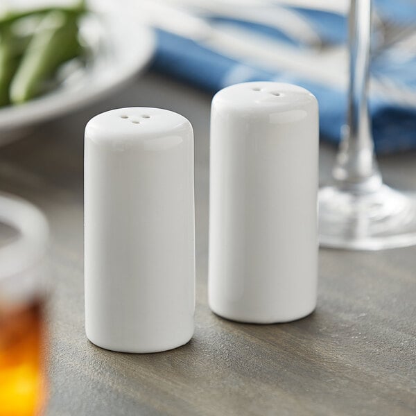 A white ceramic salt shaker with a white cap and a white ceramic pepper shaker with a black cap on a table.