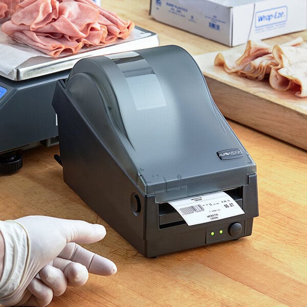 A person in a glove using an AvaWeigh label printer next to a stack of meat.