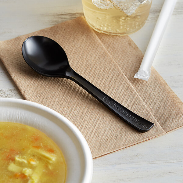A black spoon in a bowl of soup on a table with a napkin and a drink.