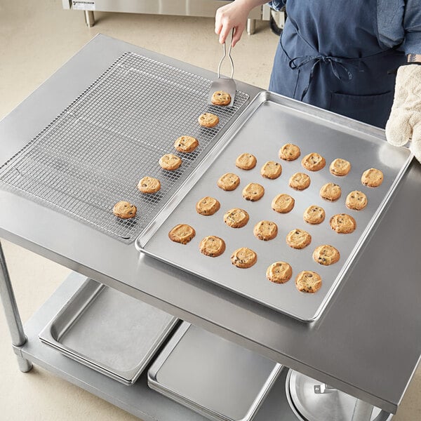 A person using a Choice wire in rim aluminum sheet pan to bake cookies on a tray.