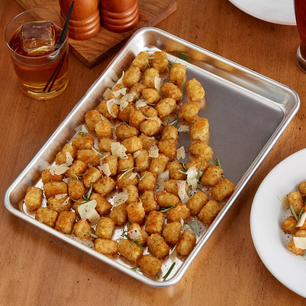 A table with a Choice quarter size aluminum bun pan of tater tots on it.