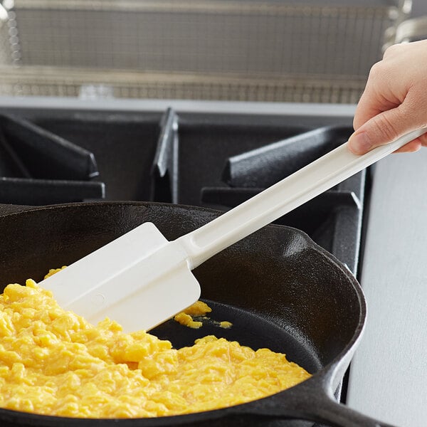 A hand using a Vollrath white plastic spatula to stir scrambled eggs in a pan.