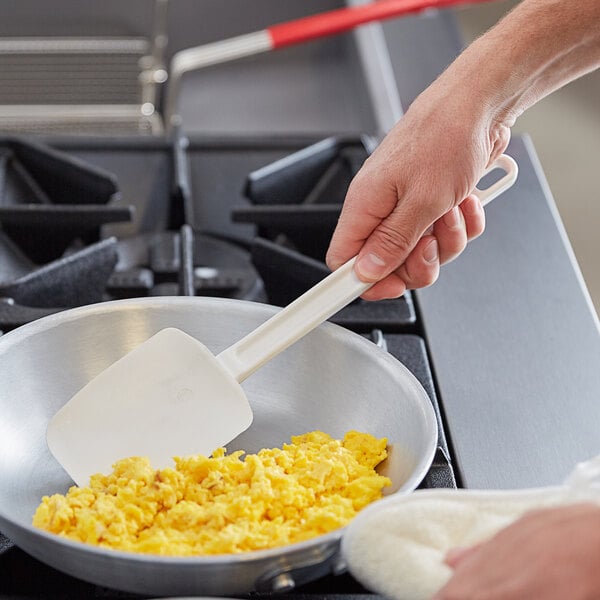 A hand using a Vollrath SoftSpoon spatula to cook scrambled eggs in a pan.