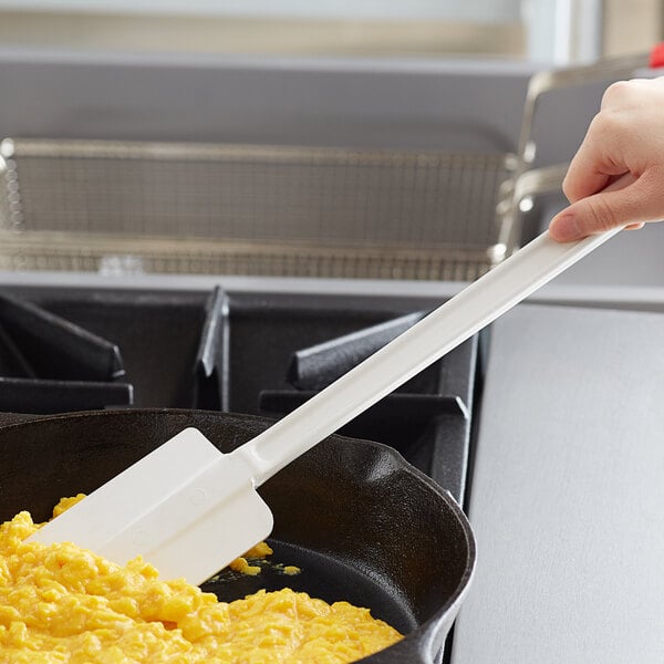 A person using a Vollrath White Plastic Spatula to stir scrambled eggs in a pan.