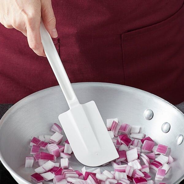A person using a white Vollrath spatula to stir chopped onions in a pan.