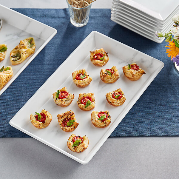 A white marble rectangular melamine platter with appetizers on a table.
