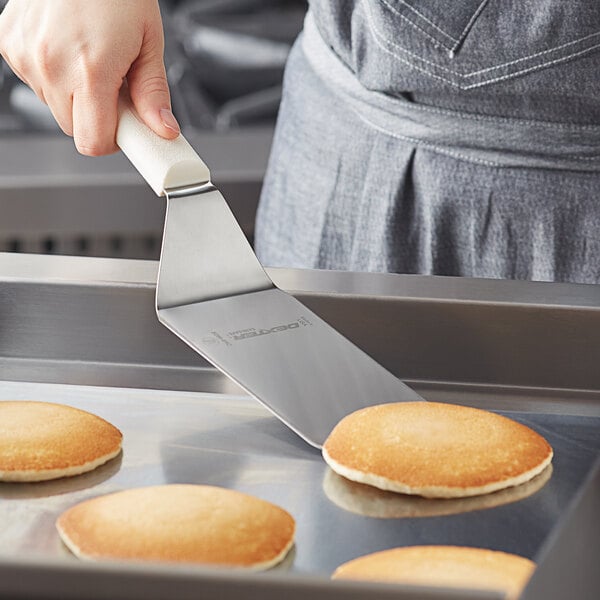 A person using a Dexter-Russell Sani-Safe round corner solid turner to cook pancakes.