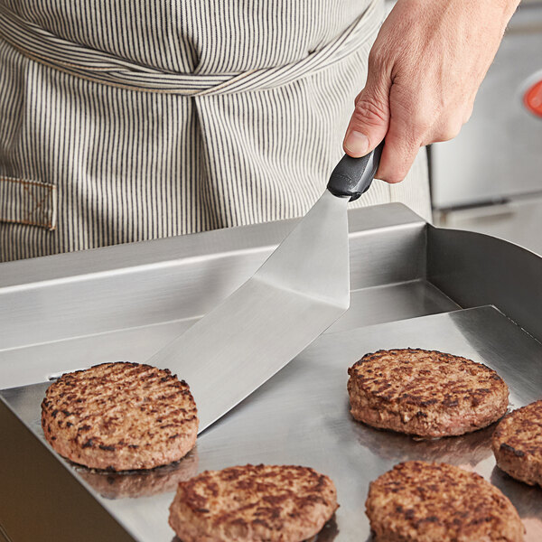 A person using a Vollrath Jacob's Pride Ergo Grip hamburger turner to cook burgers on a grill.