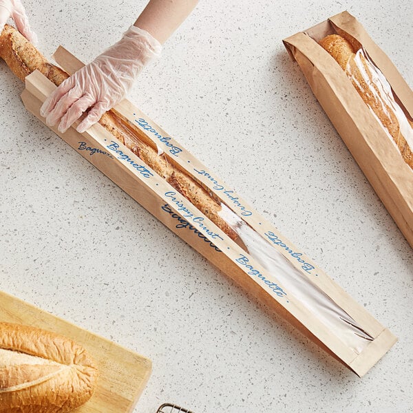 A hand wearing a glove cutting a Bagcraft Packaging EcoCraft Dubl-Panel Crispy Crust Baguette bread bag on a wooden board.