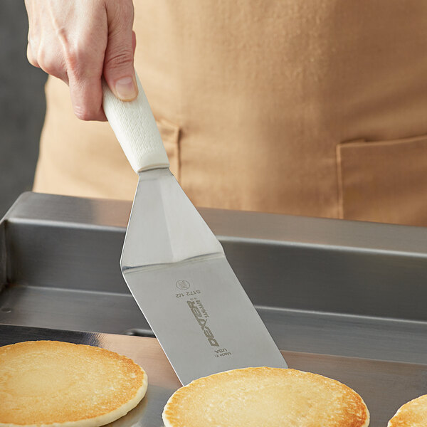 A hand using a Dexter-Russell pancake turner to flip a pancake.