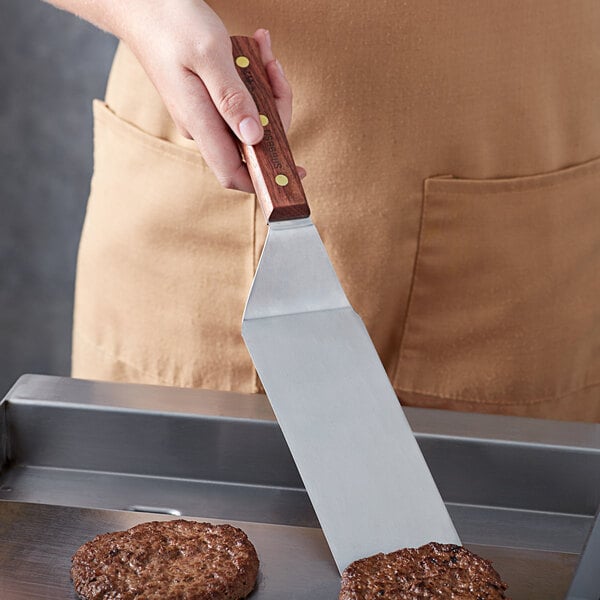 A person using a Dexter-Russell large square hamburger turner to cut a burger.