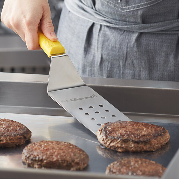 A person using a Dexter-Russell yellow perforated turner to put food on a burger.
