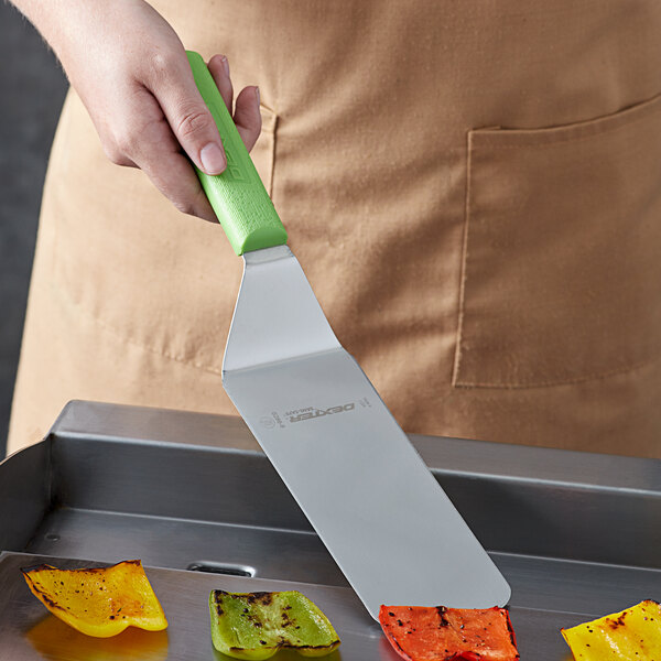 A person holding a Dexter-Russell Sani-Safe solid turner with a green handle over peppers.