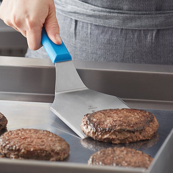 A person using a Dexter-Russell blue solid hamburger turner to grill hamburgers.