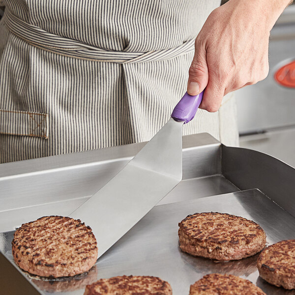 A person using a Vollrath Jacob's Pride Hamburger Turner with a purple handle to cook burgers.