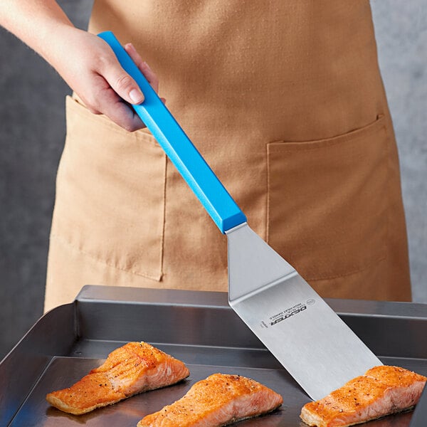 A person using a Dexter-Russell Cool Blue Basics long handle solid turner to cook salmon on a pan.