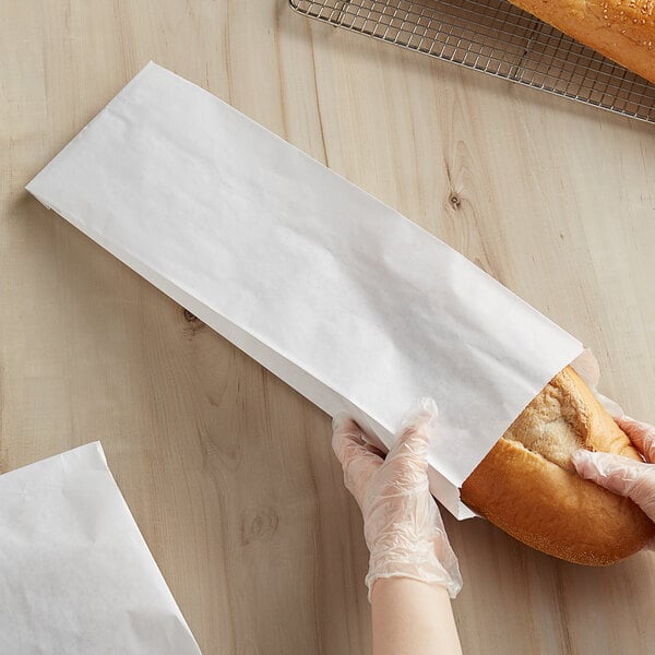 A person wearing plastic gloves holding a Bagcraft white bread bag full of loaves.