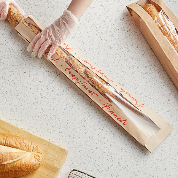 A person in gloves holding a Bagcraft Packaging EcoCraft Dubl-Panel French bread bag with a long loaf of bread.