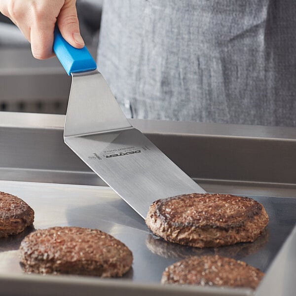 A person using a Dexter-Russell blue square edge turner to cook burgers.