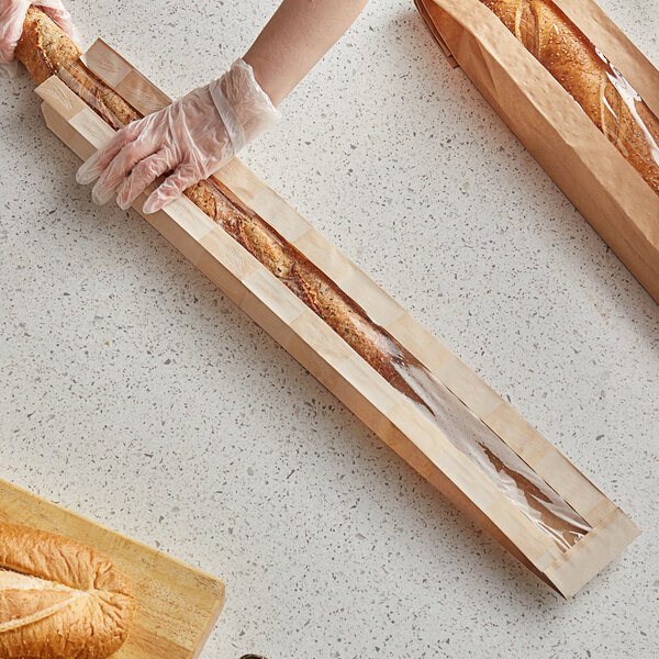 A person using a Bagcraft EcoCraft Dubl-Panel paper bag to hold a long loaf of bread.