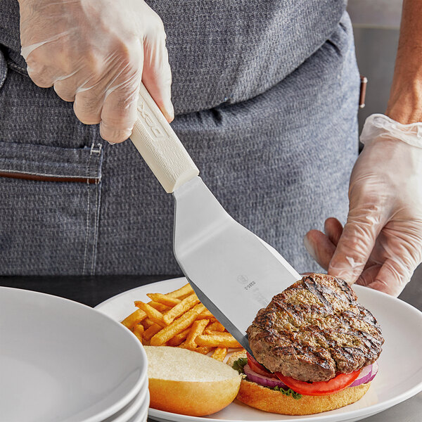 A person using a Dexter-Russell hamburger turner to cut a burger on a plate.