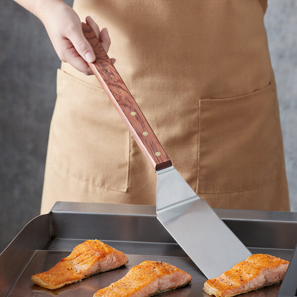 A person using a Dexter-Russell long handled solid turner to cook salmon in a pan.