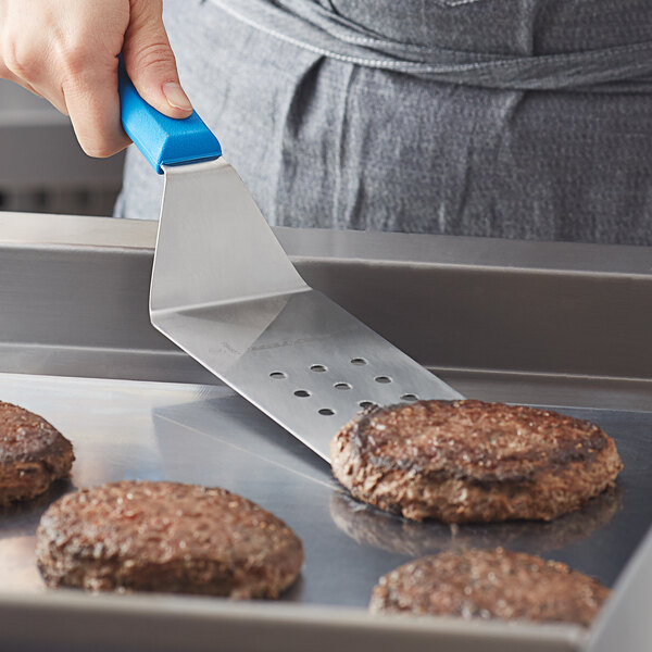 A person using a Dexter-Russell blue perforated turner to cook burgers.