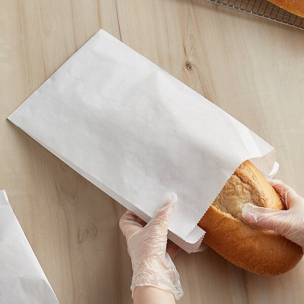 A person in gloves holding a loaf of bread in a Bagcraft Packaging white bread bag.