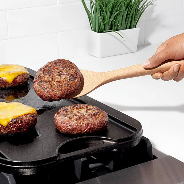 A person using an OXO Good Grips wooden spatula to flip burgers on a grill.